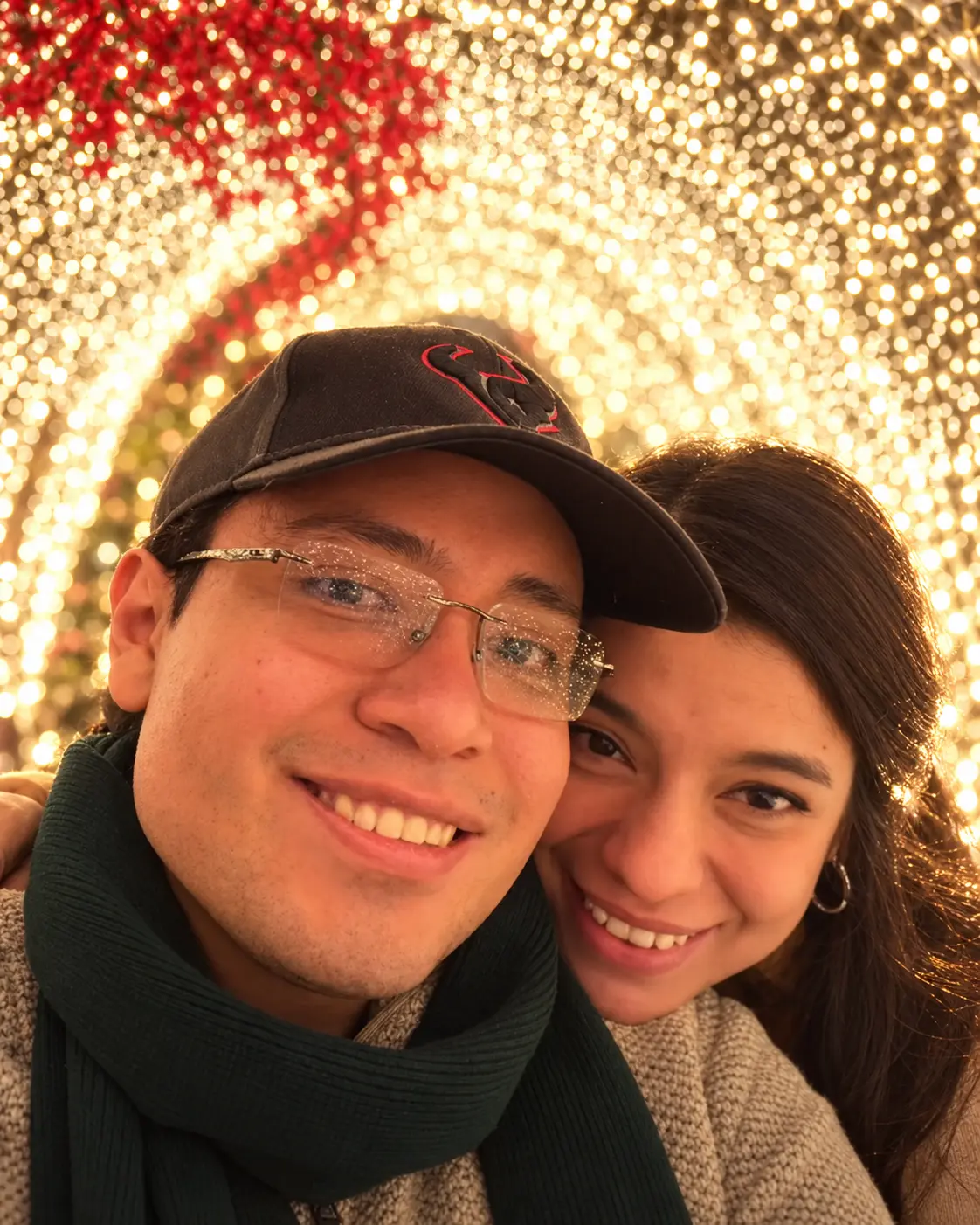 Andrea y Vladimir sonriendo juntos bajo una instalación de luces cálidas