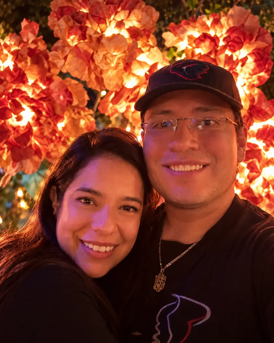 Andrea y Vladimir abrazados frente a un fondo floral iluminado